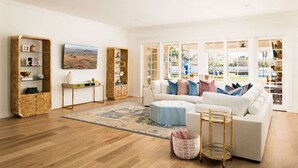 A spacious living room with a white sofa, a wooden console table, a large window with a view, and a patterned rug. - Chateau D`Arcadia - A French Inspired Luxury Home (Scottsdale)