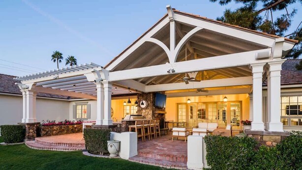 A covered patio with a stone fireplace, outdoor seating, and a well-maintained lawn. - Chateau D`Arcadia - A French Inspired Luxury Home (Scottsdale)