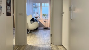A hallway leading to a living area with a modern sofa, a small table, and a view of the outdoors through large windows.