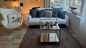 A modern living room with a sofa, a white armchair, a coffee table, and a view of a cityscape through large windows.