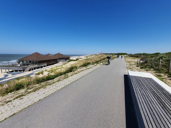 En strandpromenad med en träbrygga, strandhus och en fri utsikt över havet.