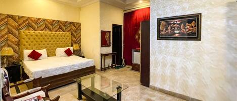 A hotel room with a large bed, a glass coffee table, a desk, and a chair.