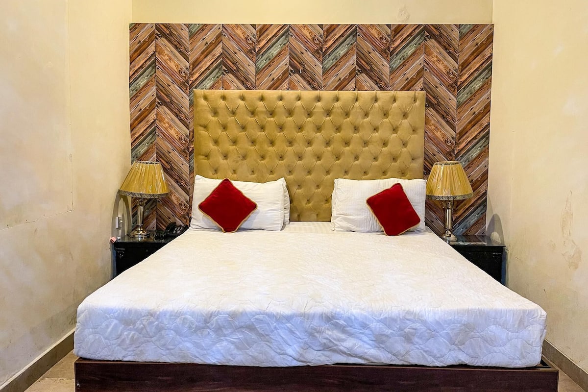 Una cama con cabecera capitonada, dos lámparas de noche y dos almohadas rojas.