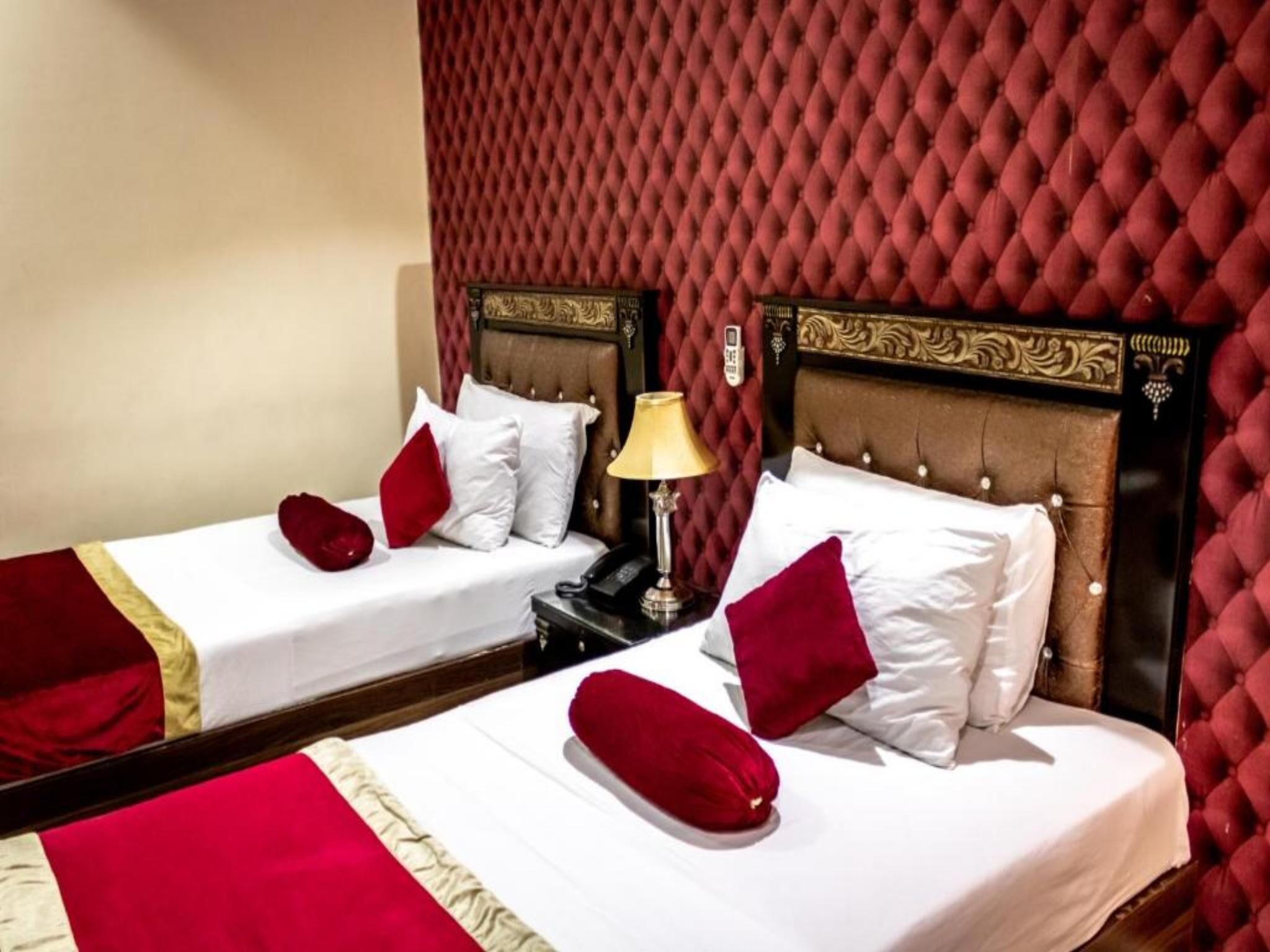 Dos camas individuales con ropa de cama roja y blanca, una mesita de noche con lámpara y una pared con estampado rojo.