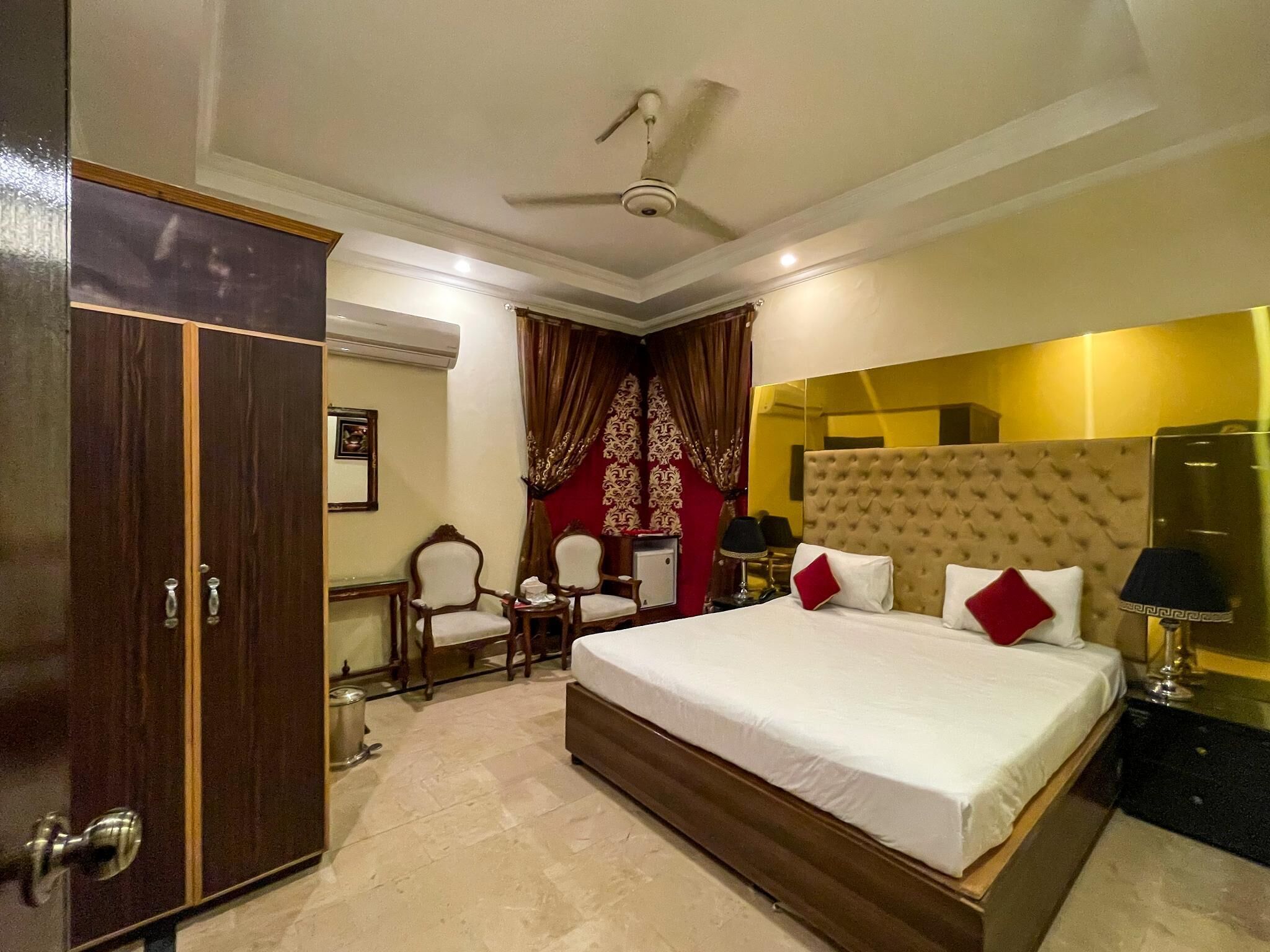 A hotel room with a large bed, a wardrobe, a desk, and a ceiling fan.