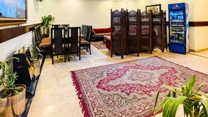 A spacious living area with a high ceiling, a ceiling fan, a large decorative light fixture, a seating area with sofas and chairs, a patterned rug, and a vending machine. - Rose Palace Hotel Gulberg (Lahore)