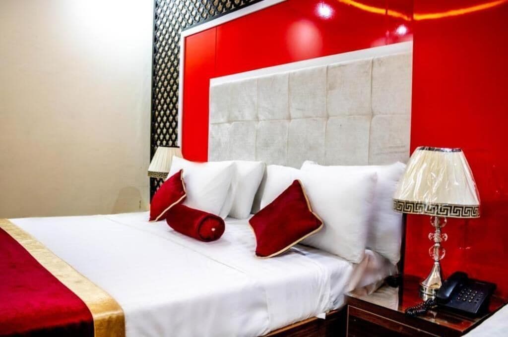 Ein Hotelzimmer mit einem großen Bett, Bettwäsche in Rot und Weiß, einem Telefon und einer Lampe auf einem Nachttisch aus Holz.