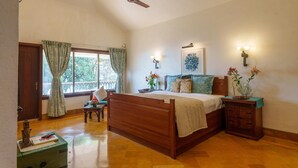 Een slaapkamer met een houten bed, nachtkastje, dressoir, raam met gordijnen, plafondventilator en wandlampen.
