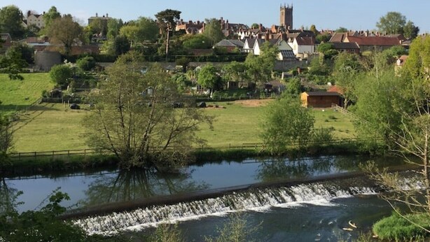 A riverside view of a town with a church tower, houses, and a lock system. - Delightful 2 bed town house in historic Ludlow. (Ludlow)