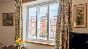 A room with a large window, floral curtains, a vase with flowers, and a framed picture on the wall. - Delightful 2 bed town house in historic Ludlow. (Ludlow)