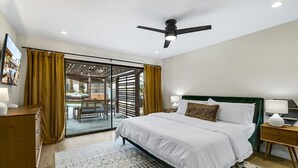 A bedroom with a bed, a nightstand, a desk, a chair, and a large window.