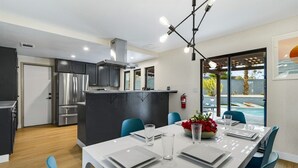 A modern kitchen with stainless steel appliances, a dining area with blue chairs, and a view of a swimming pool.