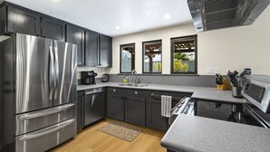 A modern kitchen with dark cabinets, stainless steel appliances, a built-in oven, and a large window providing natural light.