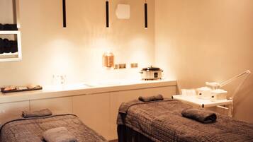 Two beds with dark-colored blankets, illuminated by pendant lights, and a comfortable workspace nearby.