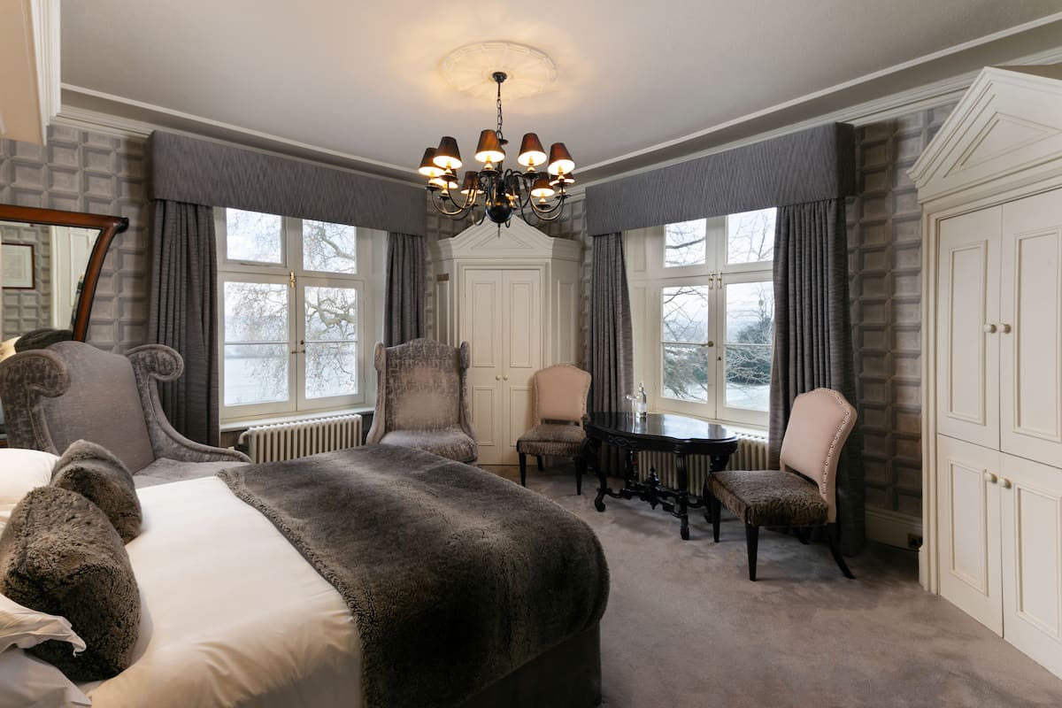 A bedroom with a large bed, two armchairs, a small table, and a chandelier.