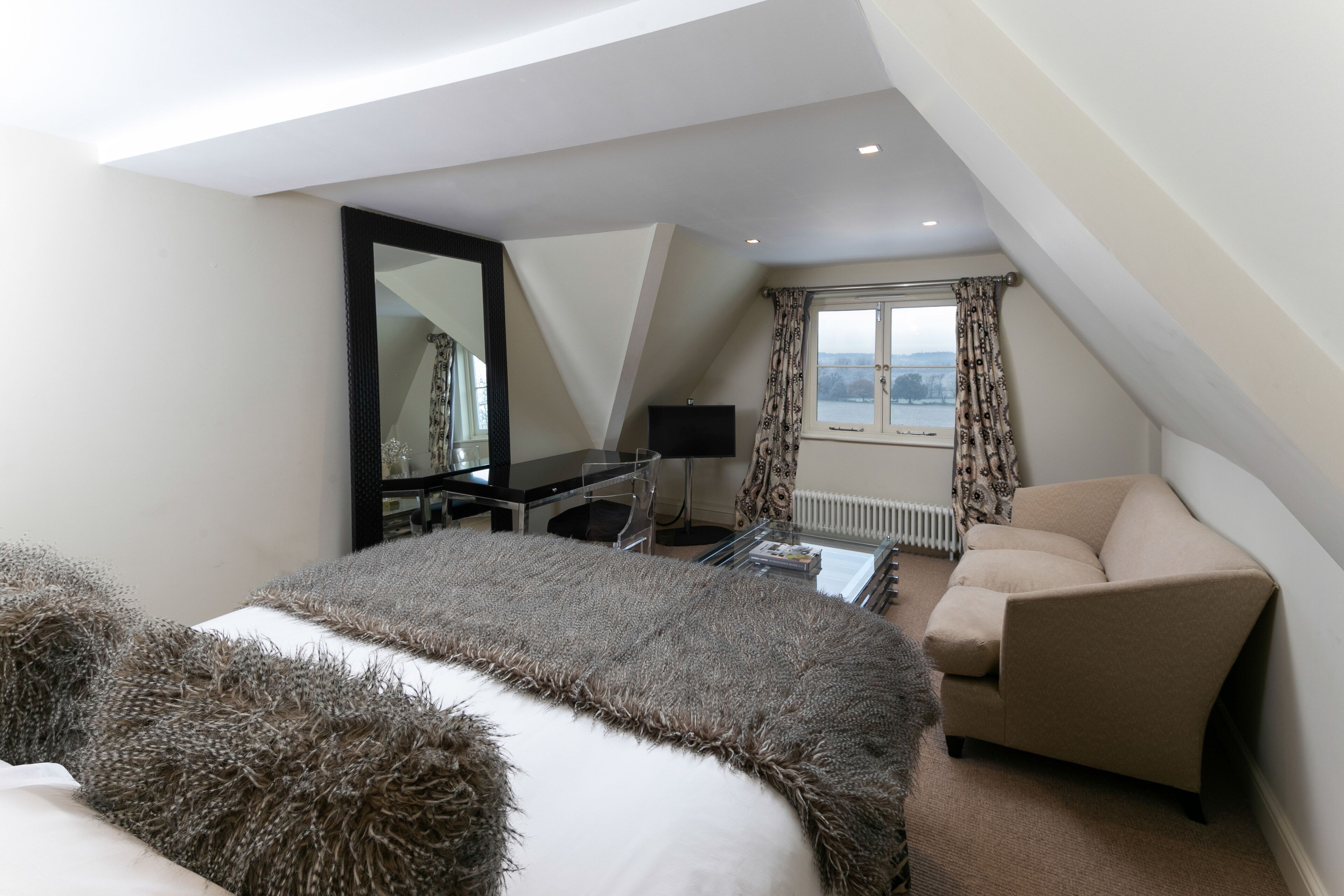 Une chambre d’hôtel moderne avec un grand lit, un canapé, un bureau avec un ordinateur et une fenêtre avec des rideaux.