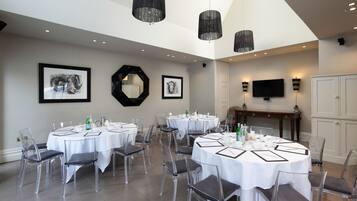 A dining area with round tables, clear chairs, and black pendant lights.