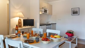 A dining area with a table set for breakfast, a TV, and a kitchen in the background. - Logis Hotel Altitude et Spa (Pexonne)