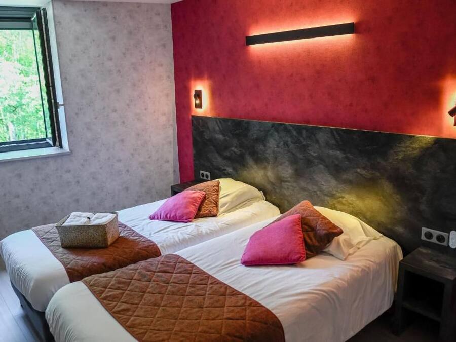 A hotel room with two beds, a large window, and a red accent wall.