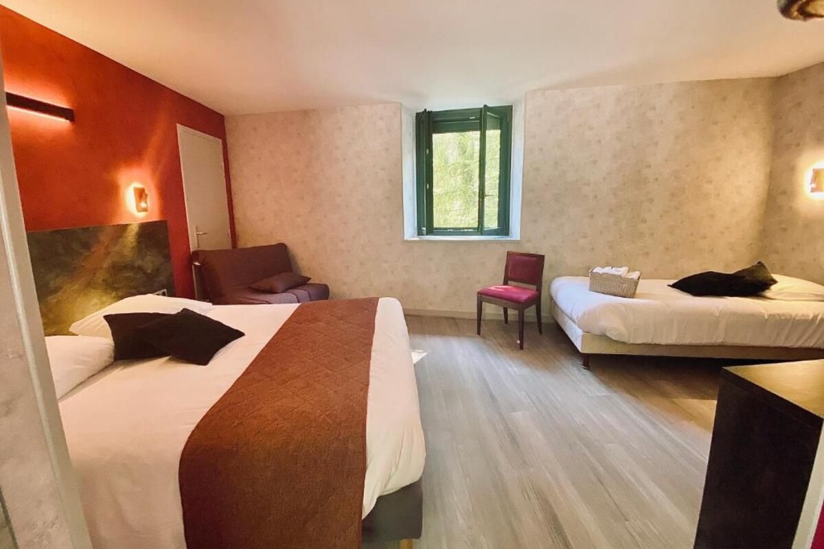 A hotel room with two beds, a chair, a small table, and a window.