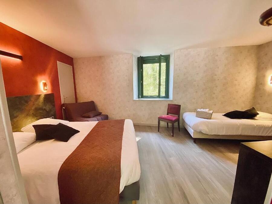 A hotel room with two beds, a chair, a small table, and a window.
