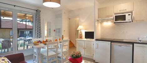 Une cuisine moderne avec des meubles blancs, un four à micro-ondes et un lave-vaisselle. On y trouve un coin repas avec une table et des chaises, ainsi qu’un canapé agrémenté d’un coussin à pois.