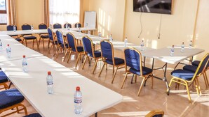 A conference room with long tables, blue upholstered chairs, and water bottles on each table.