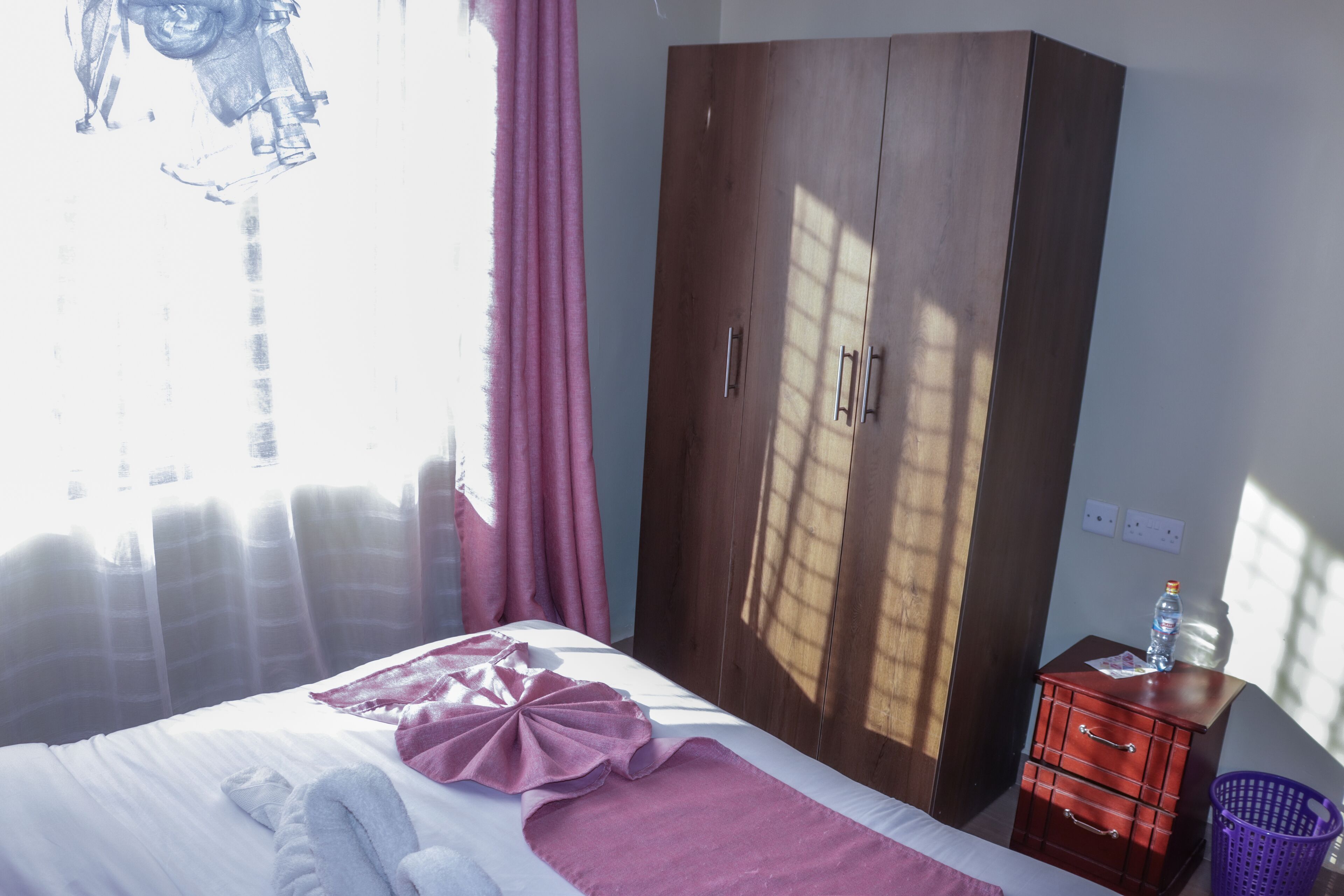 A bedroom with a bed, a wardrobe, a nightstand, and a window with curtains.