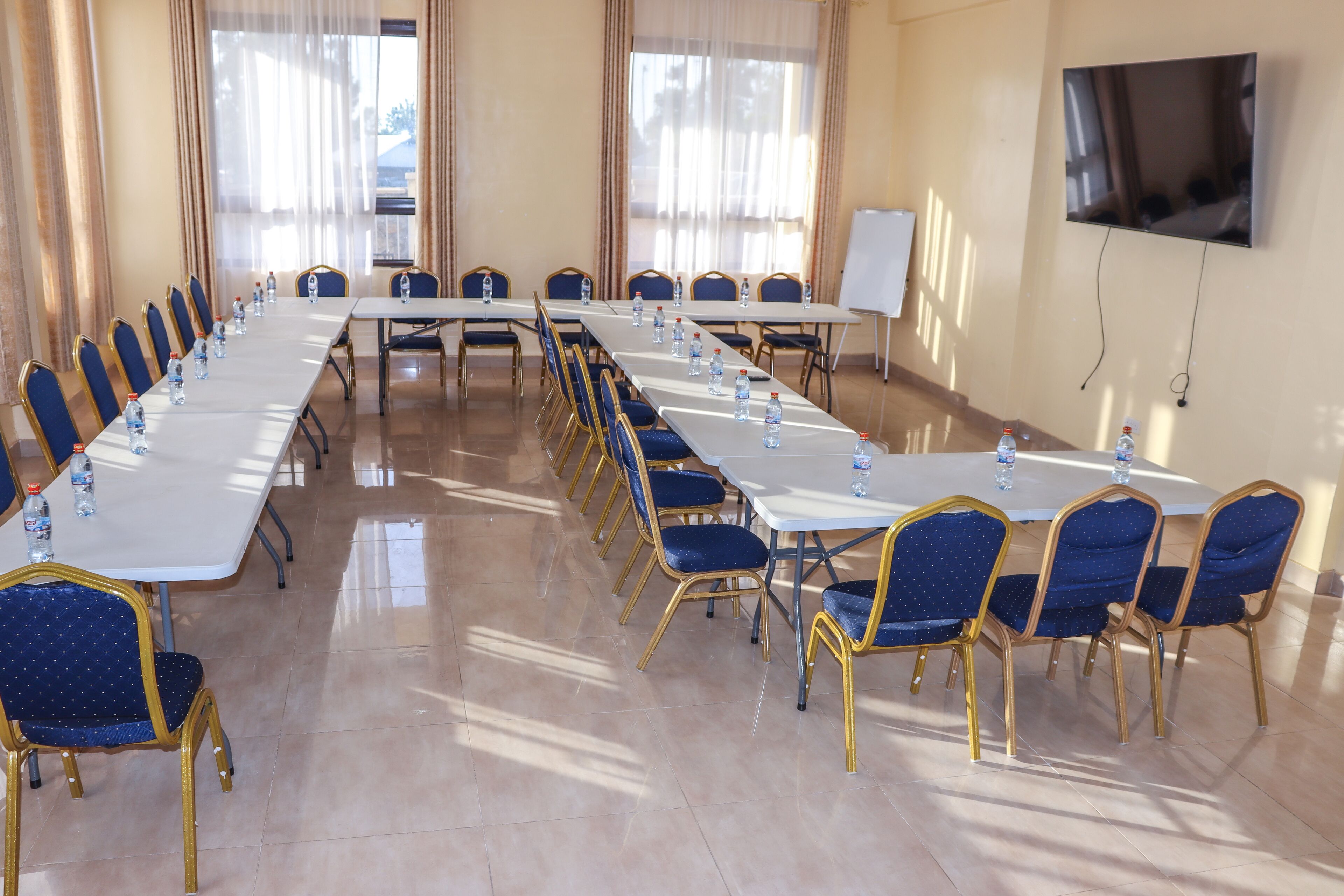 Un salón de conferencias con mesas largas, sillas azules y botellas de agua.