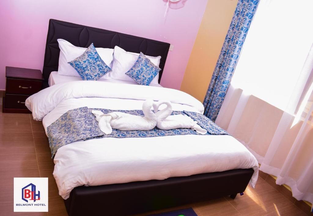 Un lit bien fait, avec des draps blancs et des coussins à motifs floraux bleus, une tête de lit sombre et une paire de serviettes disposées sur le lit.