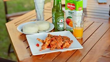 Una mesa de madera con un plato de comida, una botella de cerveza Heineken, un cartón de jugo de mango Del Monte y un vaso de jugo de naranja.