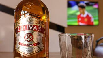 Una botella de whisky Chivas Regal y un vaso vacío sobre una mesa de madera.