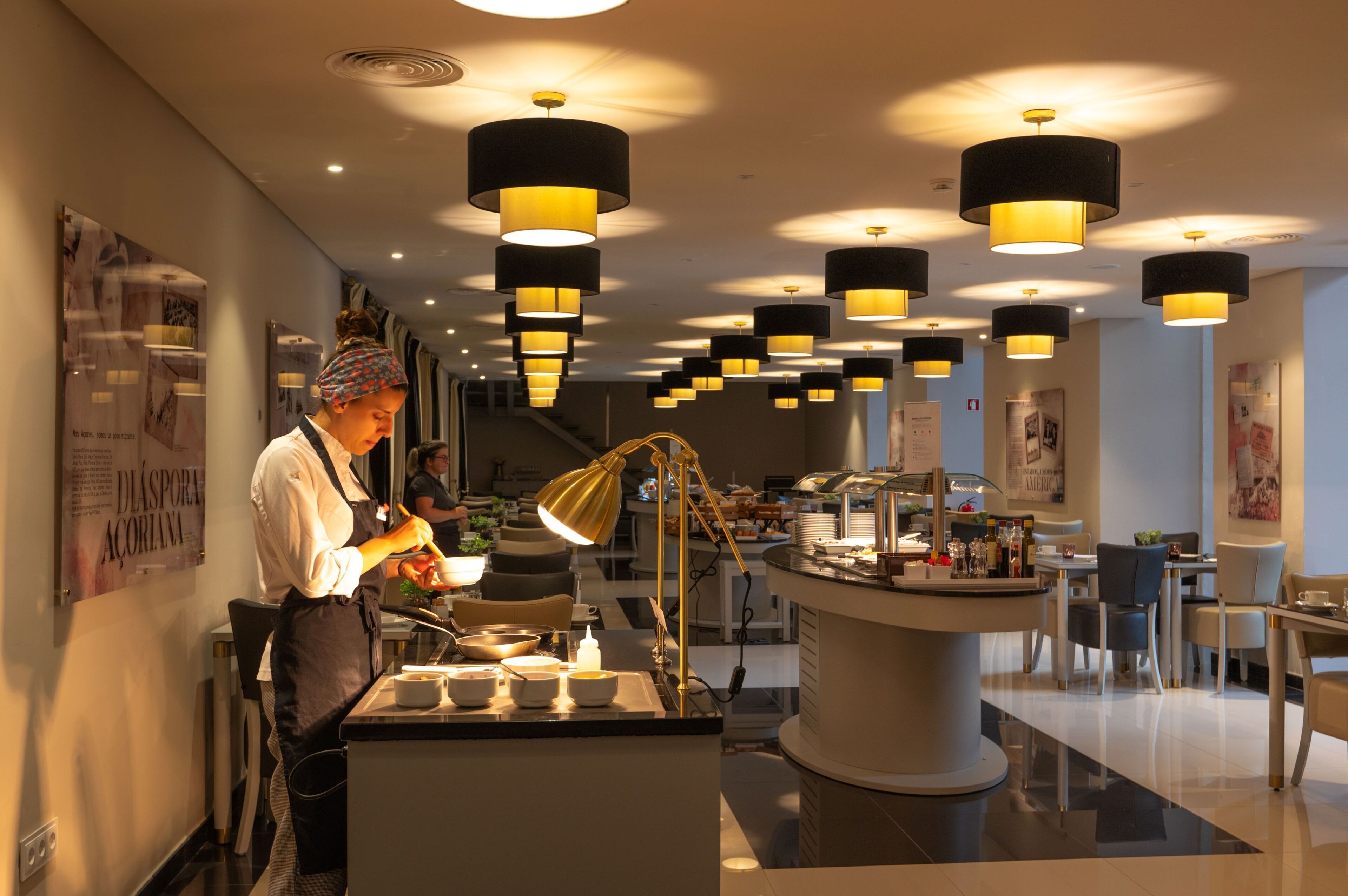 A modern restaurant with a central serving counter, overhead pendant lighting, and a clean, contemporary interior design.