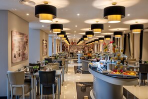 A modern hotel dining area with multiple tables, black and gold pendant lights, and a buffet counter with various food items. - Vila Gale Collection S. Miguel Hotel (Ponta Delgada)