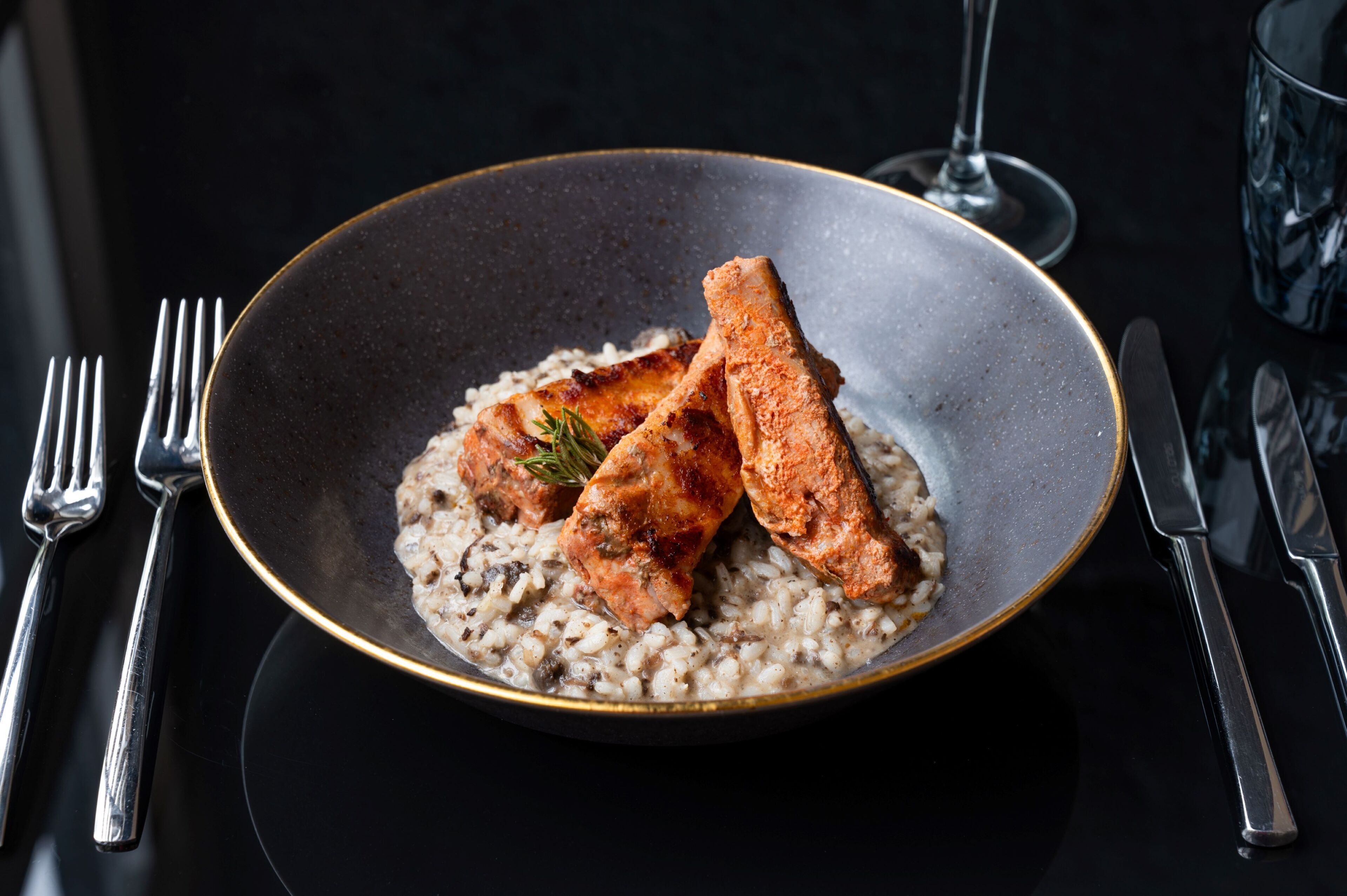 Un plato de salmón y risotto sobre una mesa oscura, con cubiertos.