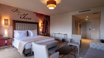 A hotel room with a large bed, a sofa, a coffee table, and a desk. There is a wall with a mural and a sign that reads "Perro de Teive".