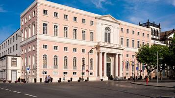 A large, pink building with a central entrance, multiple windows, and a flagpole.