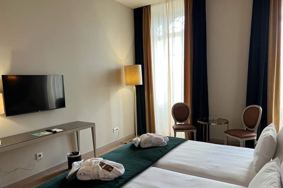 A hotel room with two beds, a TV, a desk, a lamp, and a chair.