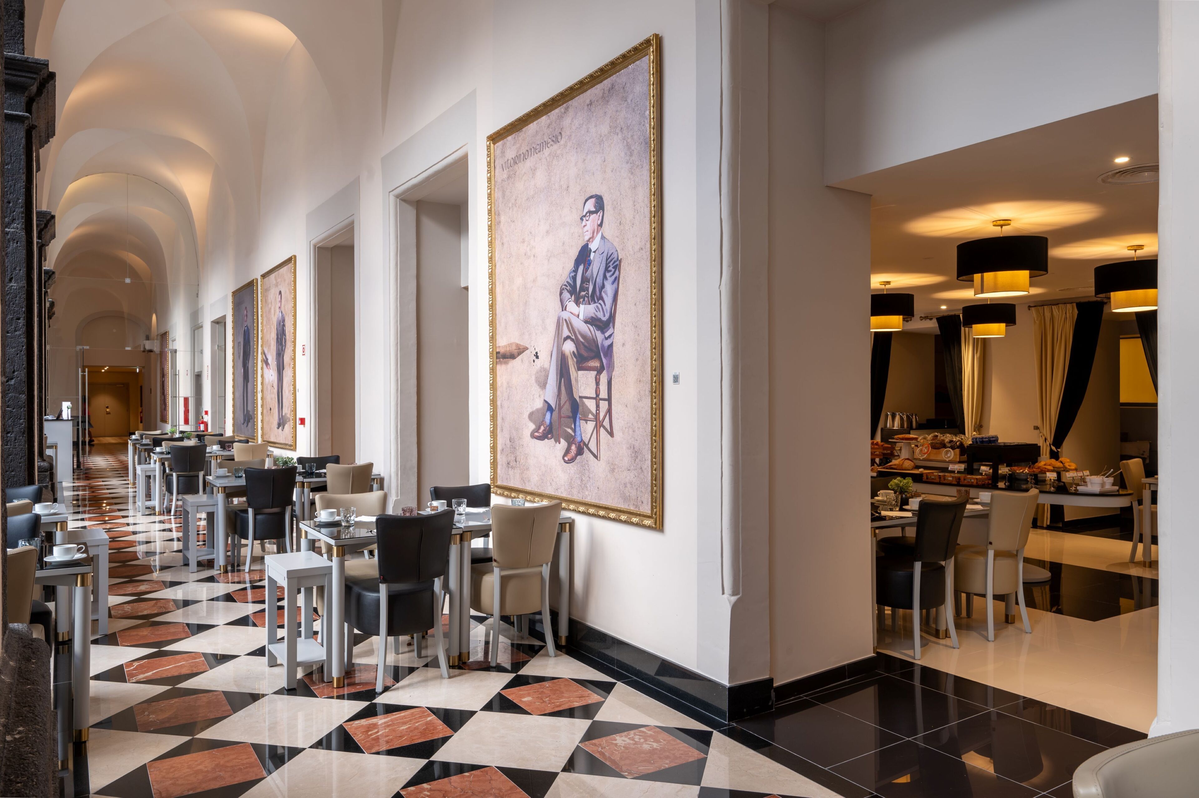 Un hall d’hôtel avec un long couloir, un espace repas et un grand tableau accroché au mur.