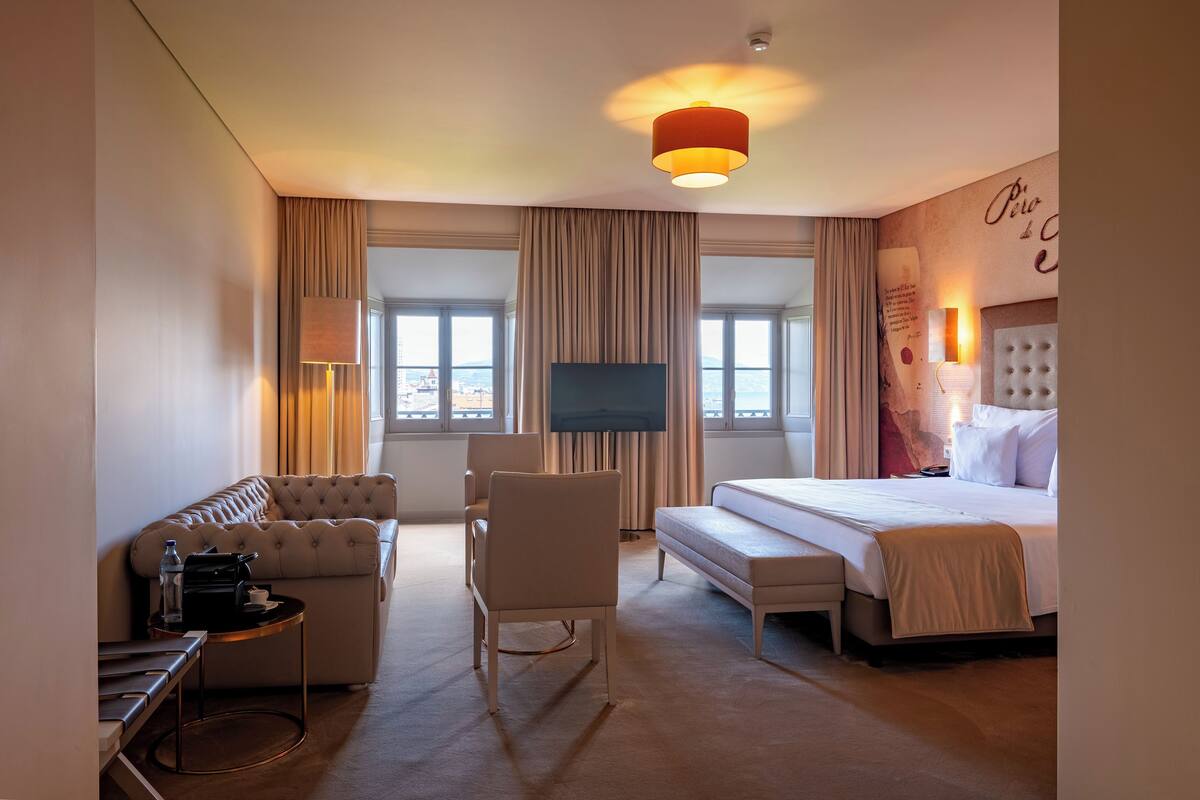 A hotel room with a bed, a sofa, a chair, a TV, and a small table.