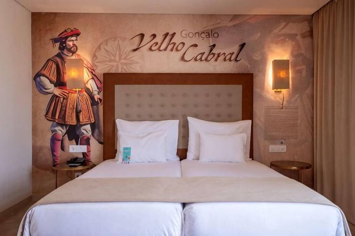 Una cama doble con cabecera, un mural en la pared y una mesita de noche con lámpara.
