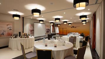 Un salón de conferencias con varias mesas redondas, cada una con sillas y vasos, y una pantalla de proyector al fondo.
