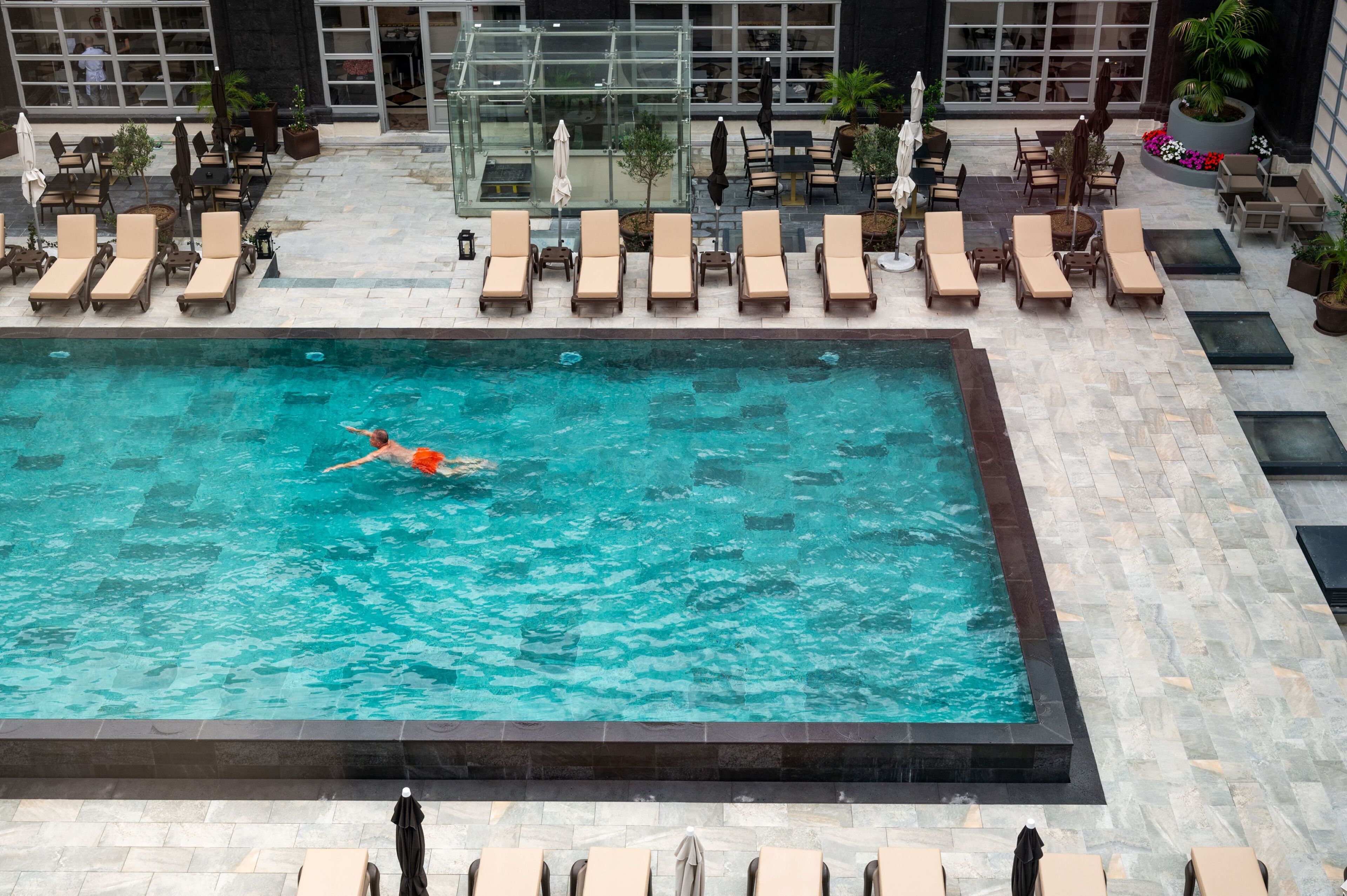 Piscina con sillas de descanso y sombrillas, rodeada de un patio con baldosas.