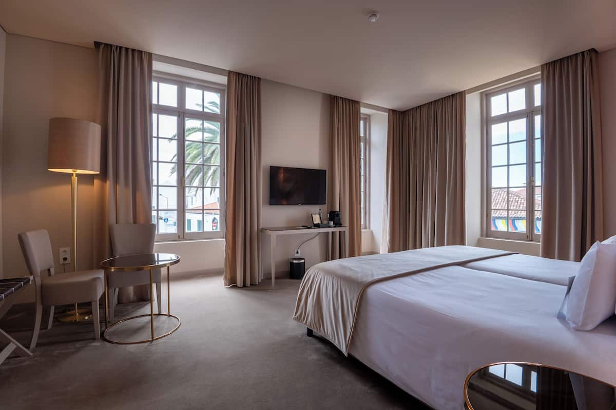 A hotel room with a large bed, a desk with a TV, a chair, and a lamp.