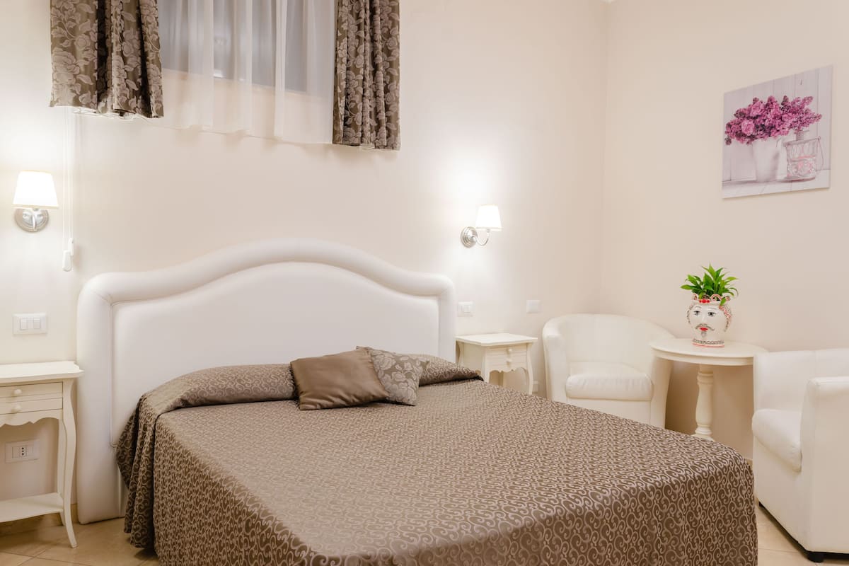 A bedroom with a bed, bedside tables, a chair, a small table with a plant, and a wall-mounted lamp.