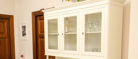 A white dining area with a round table and two chairs, a white cabinet with glass doors, and a small potted plant on top.