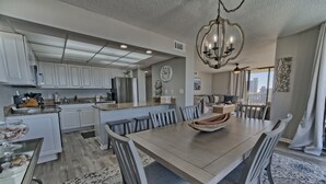 A modern kitchen with white cabinets, a large island, and a dining area with a wooden table and gray chairs.