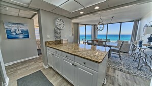 A kitchen with a large island, a dining area with a view of the ocean, and a clock on the wall.