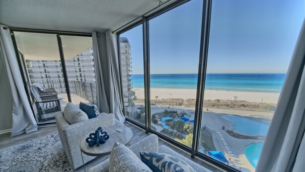 A spacious balcony with a view of a beach and a pool.
