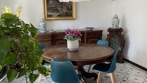 Un coin repas avec une table ronde en bois, des chaises bleues, un vase blanc orné de fleurs et un luminaire suspendu.